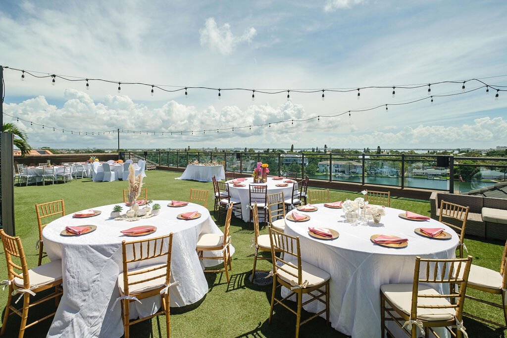 Rooftop reception with round tables, gold chiavari chairs, coral napkins and bistro string lights