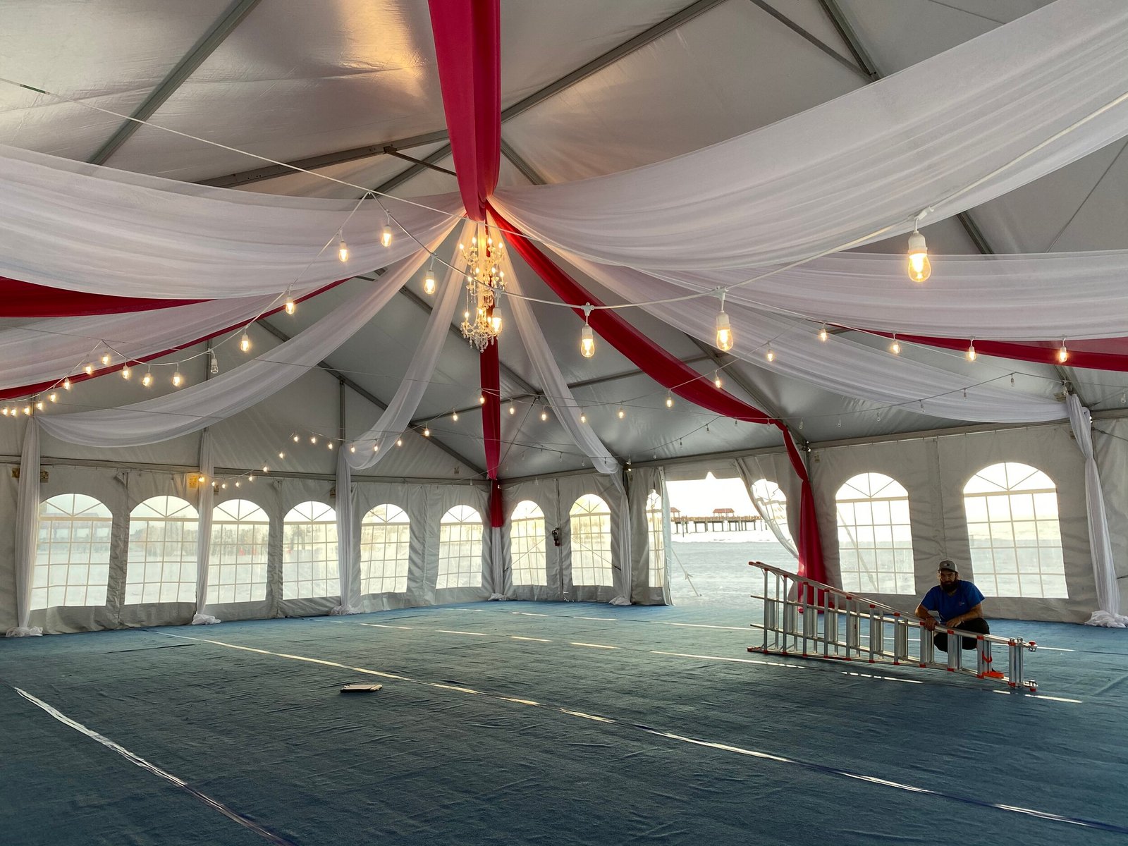 Tent interior with red and white ceiling draping, warm string lights and arched windows