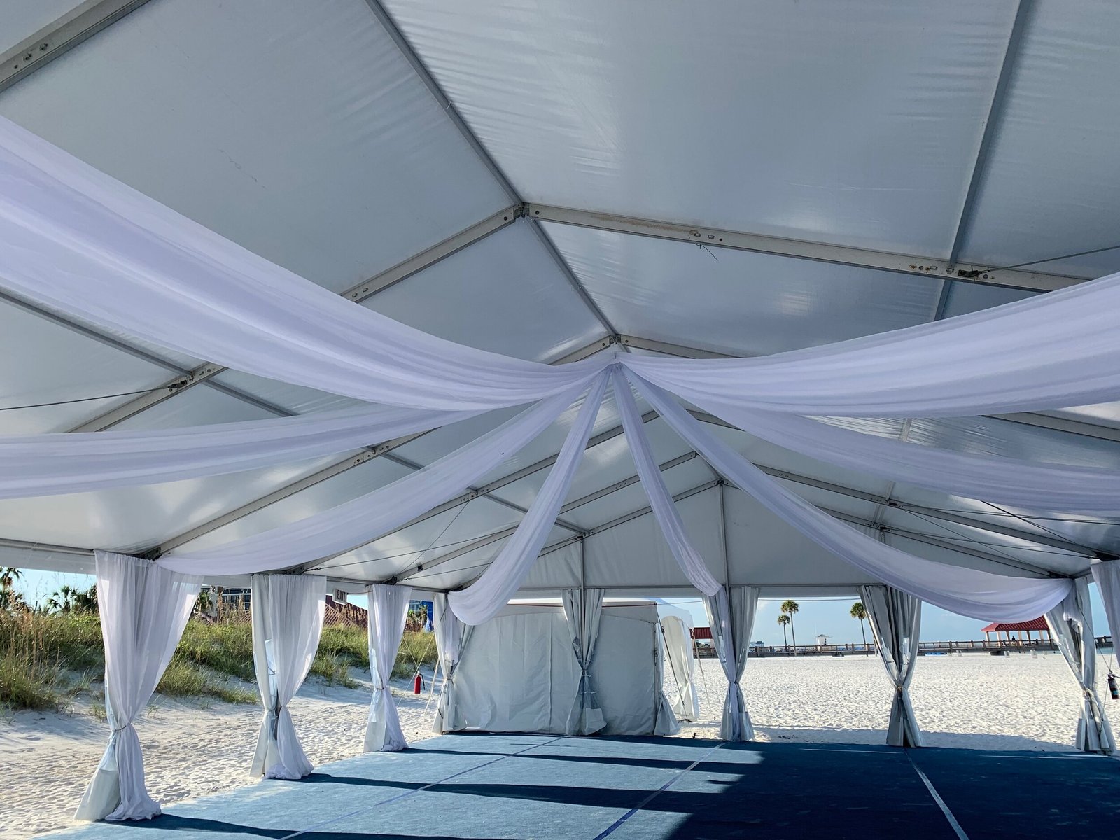 White frame tent on the sand with draped legs opening to the beach and water