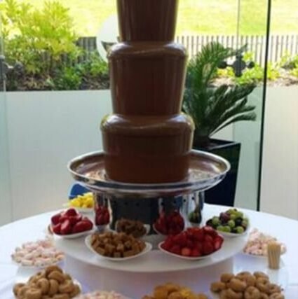 Tiered chocolate fountain surrounded by bowls of fruit and pastries for dipping