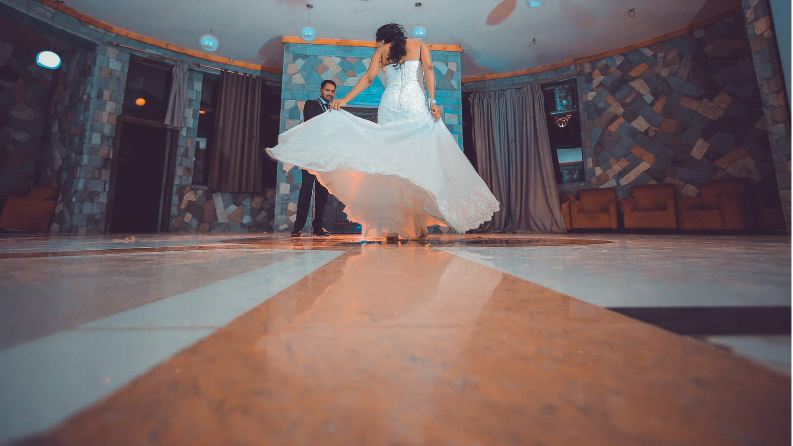 Bride in a white gown twirling on a polished dance floor as the groom watches