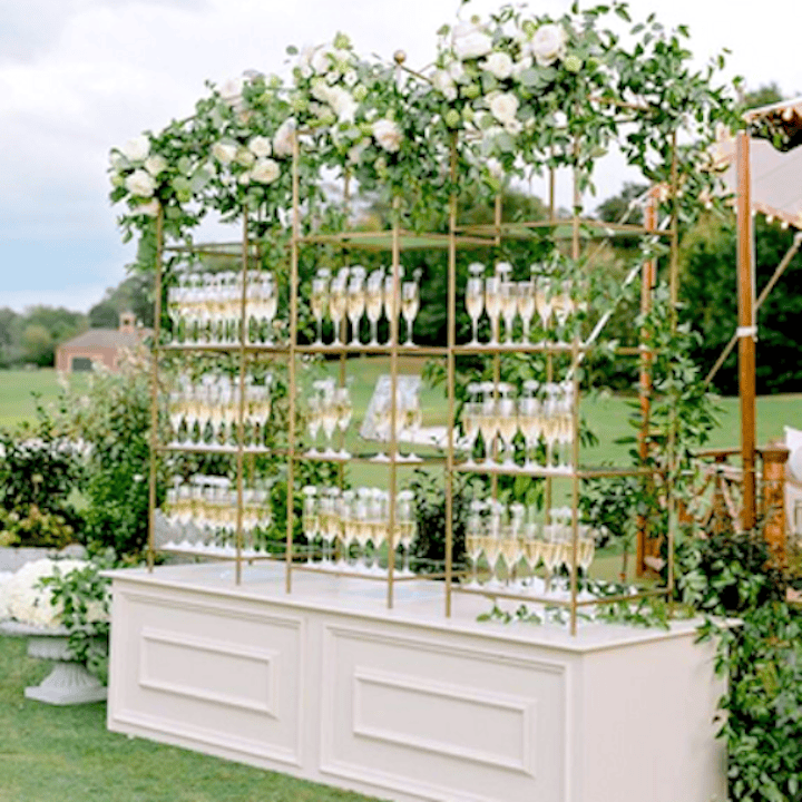 Champagne Wall and Bar Display | Gabro Event Services Elegant champagne wall with gold framing, floral accents, and greenery designed by Gabro Event Services in Tampa Bay.