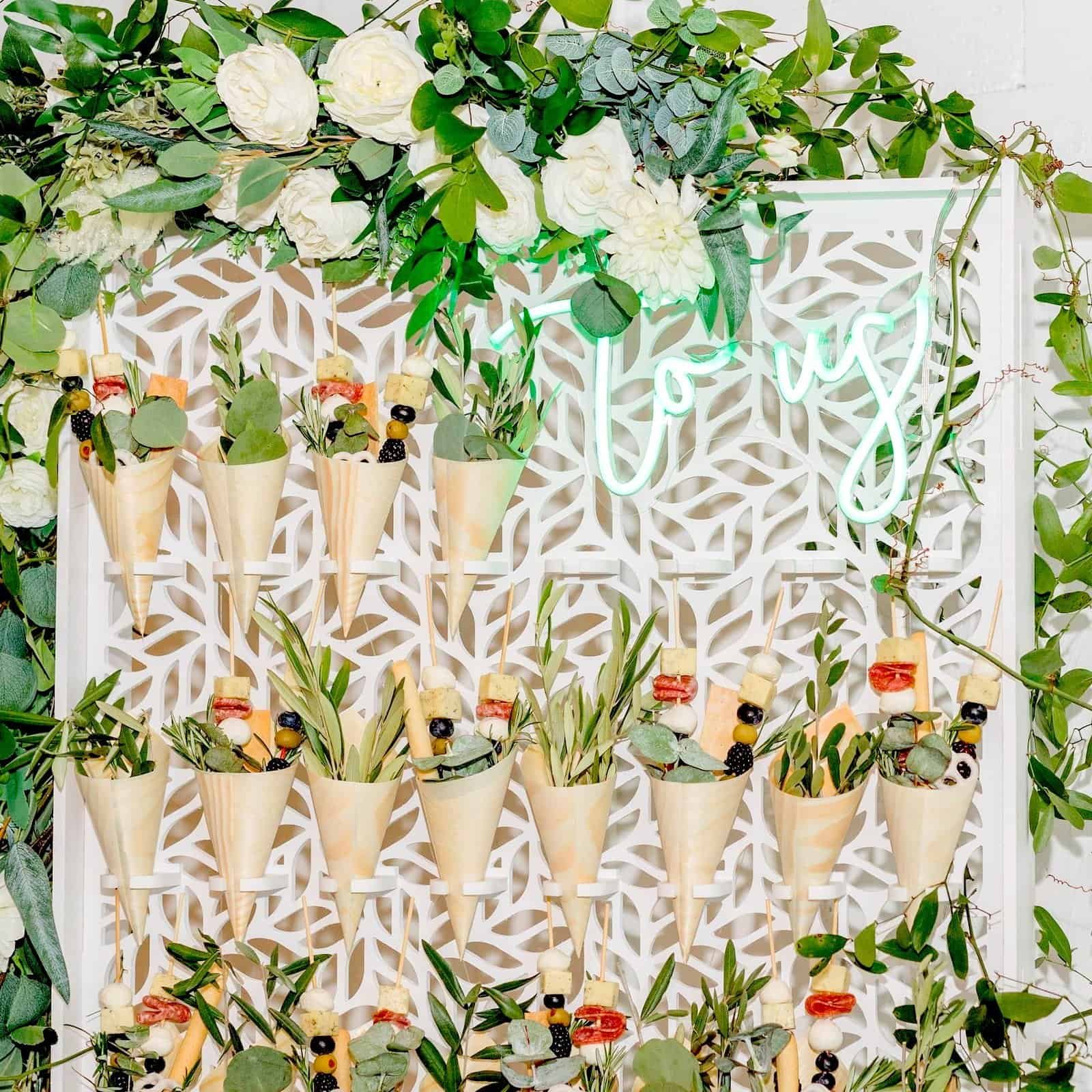 Snack cone display wall filled with paper cones, greenery and white florals