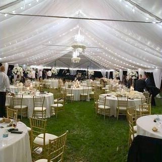 Evening tent reception on grass with warm string lights, round tables and gold chiavari chairs