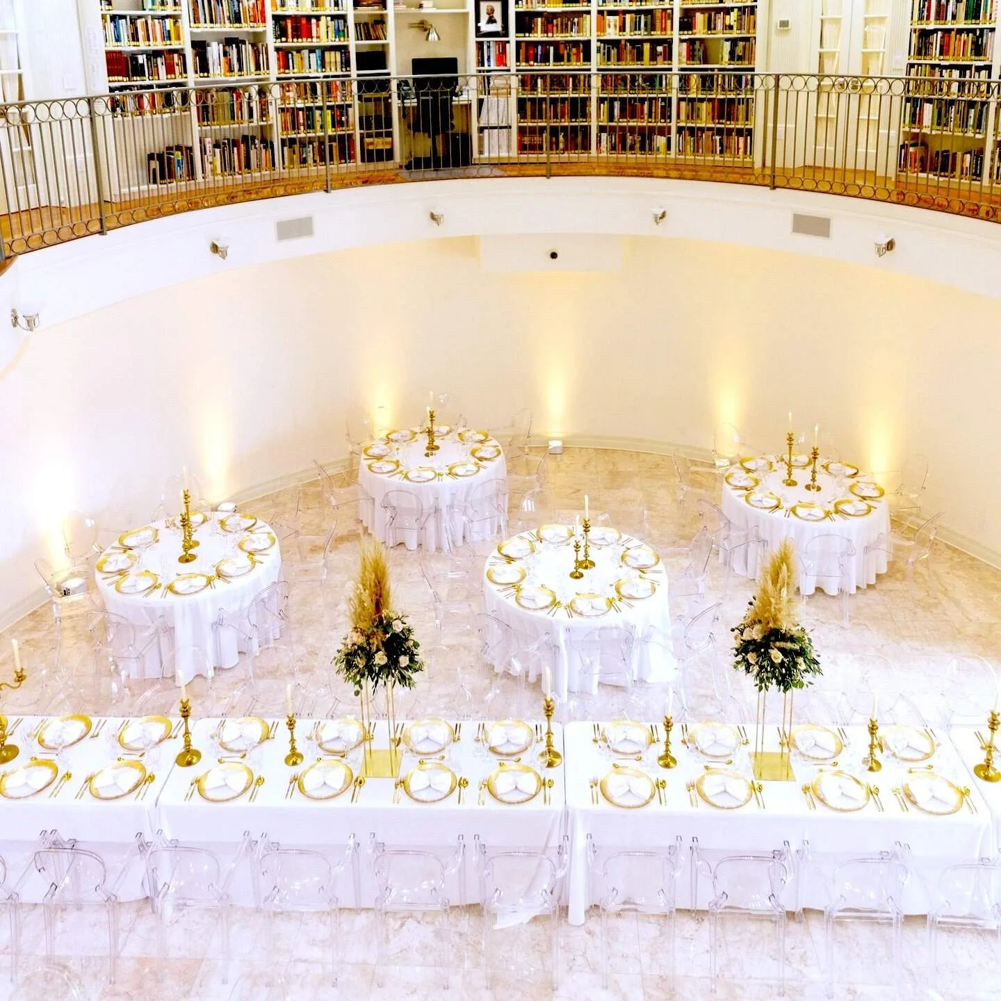 Upper level of bookshelves above lower level of fancy tables with white and gold place settings