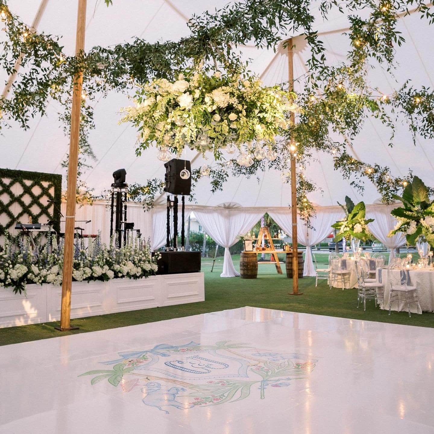 Sailcloth tent lit with string lights and hanging glass globes above a white dance floor with a custom monogram