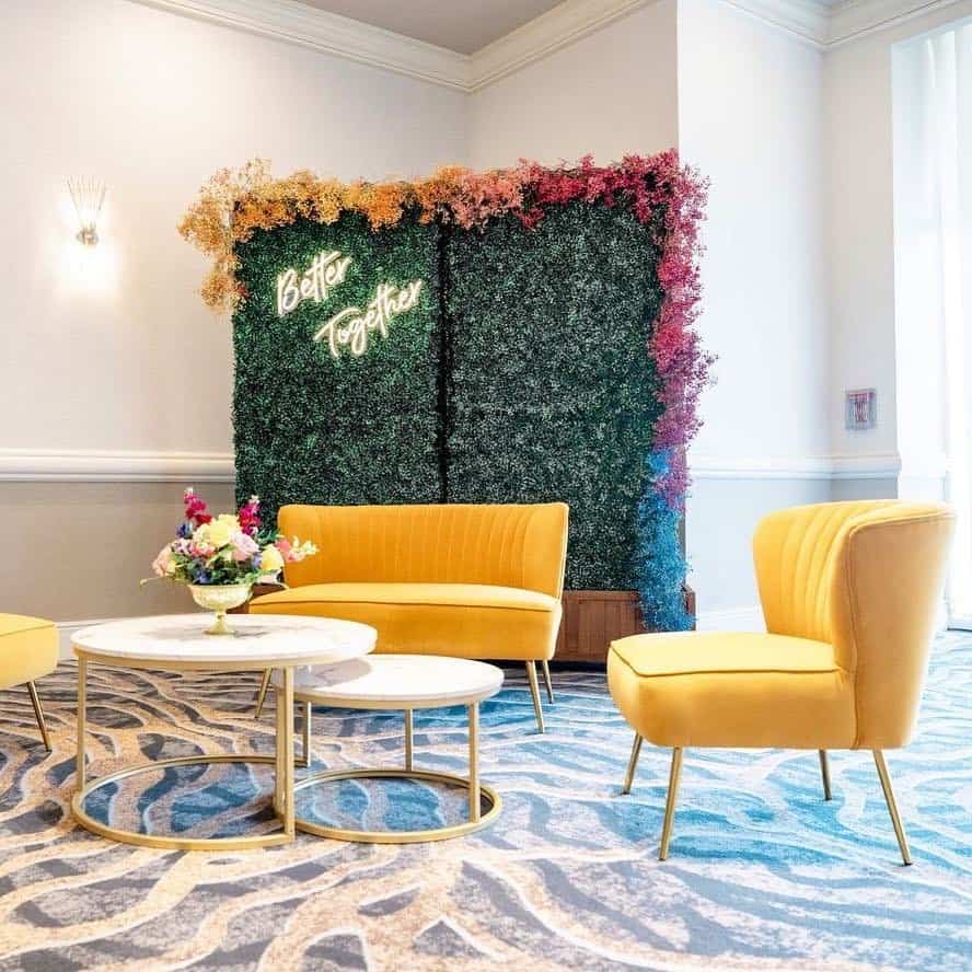 Yellow Velvet Lounge with Boxwood Backdrop and Neon Sign Yellow velvet event lounge set with floral boxwood wall and neon “Better Together” sign.