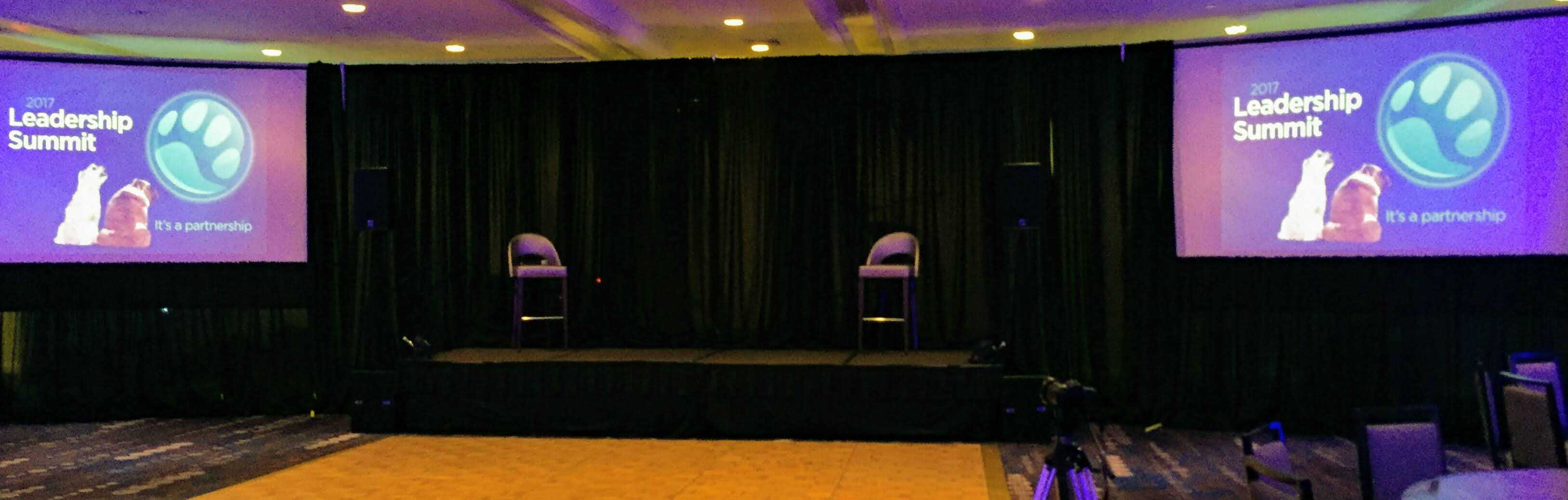 Corporate Stage and AV Setup | Gabro Event Services Corporate event stage setup with dual screens, black draping, and seating at a Tampa Bay leadership summit.