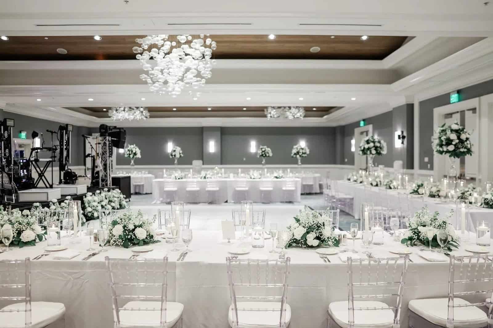Monochromatic white ballroom wedding reception with clear chiavari chairs and tall white centerpieces