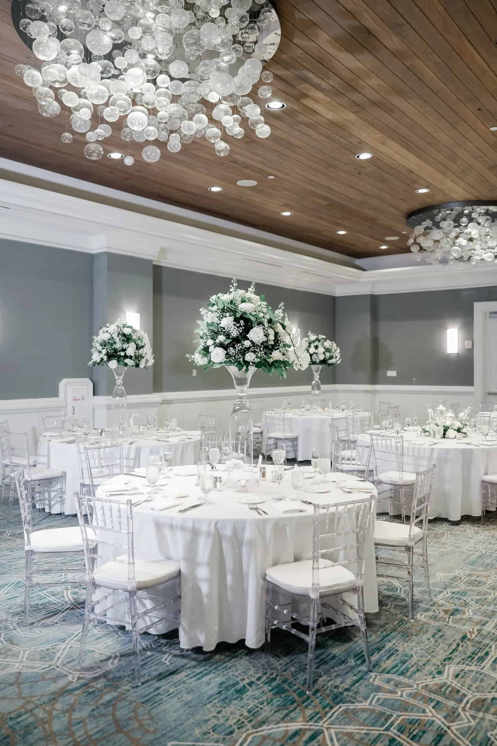 White ballroom wedding reception with clear chiavari chairs and candlelit tables