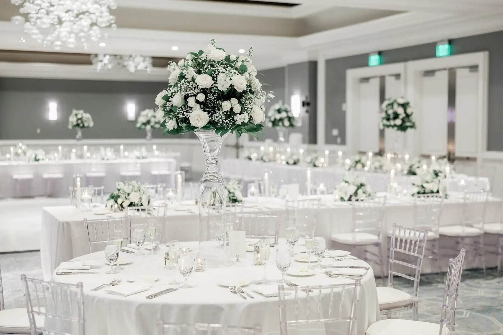 White ballroom reception with draped walls, clear chiavari chairs and tall white centerpieces