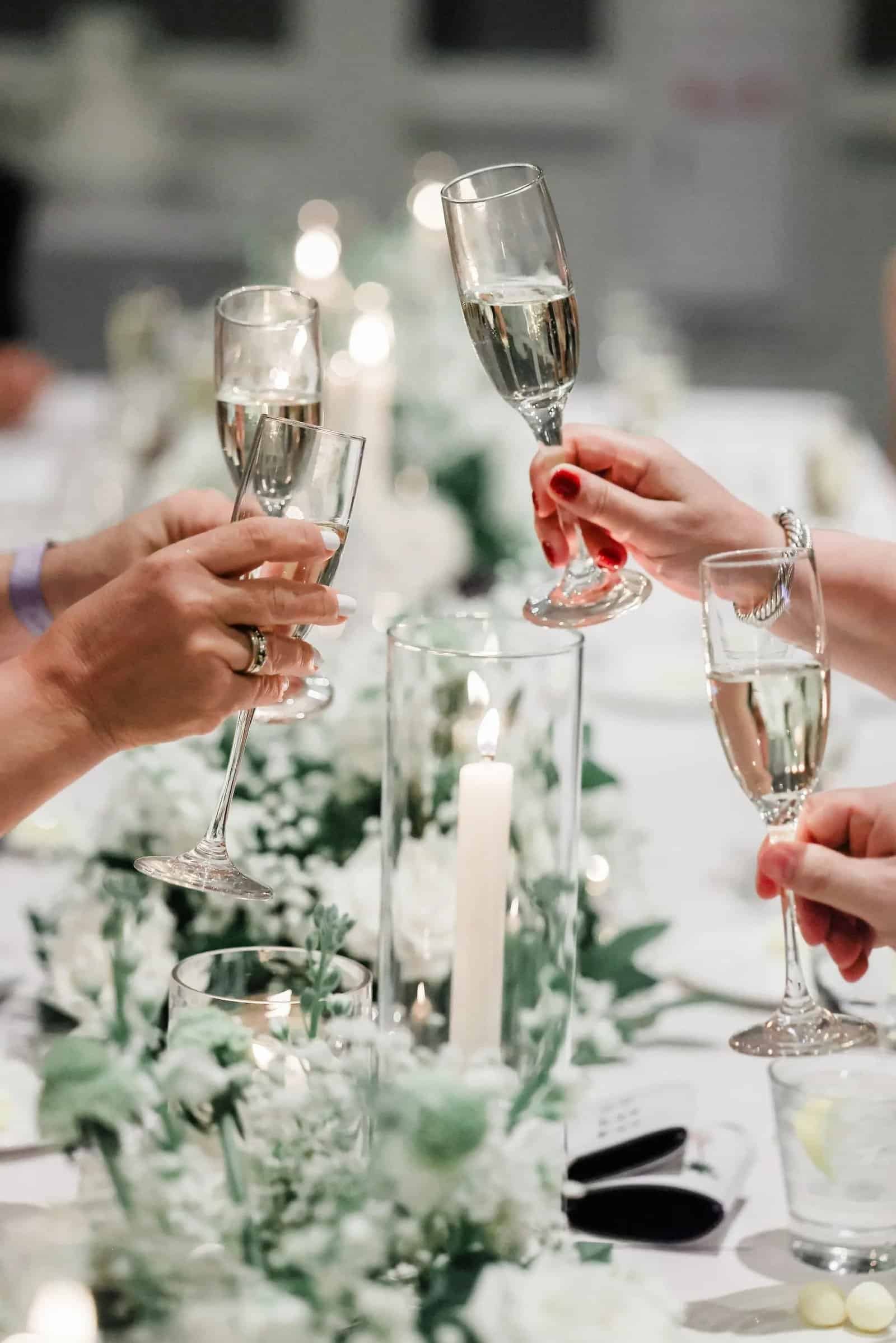 Champagne toast over a candlelit white wedding tablescape