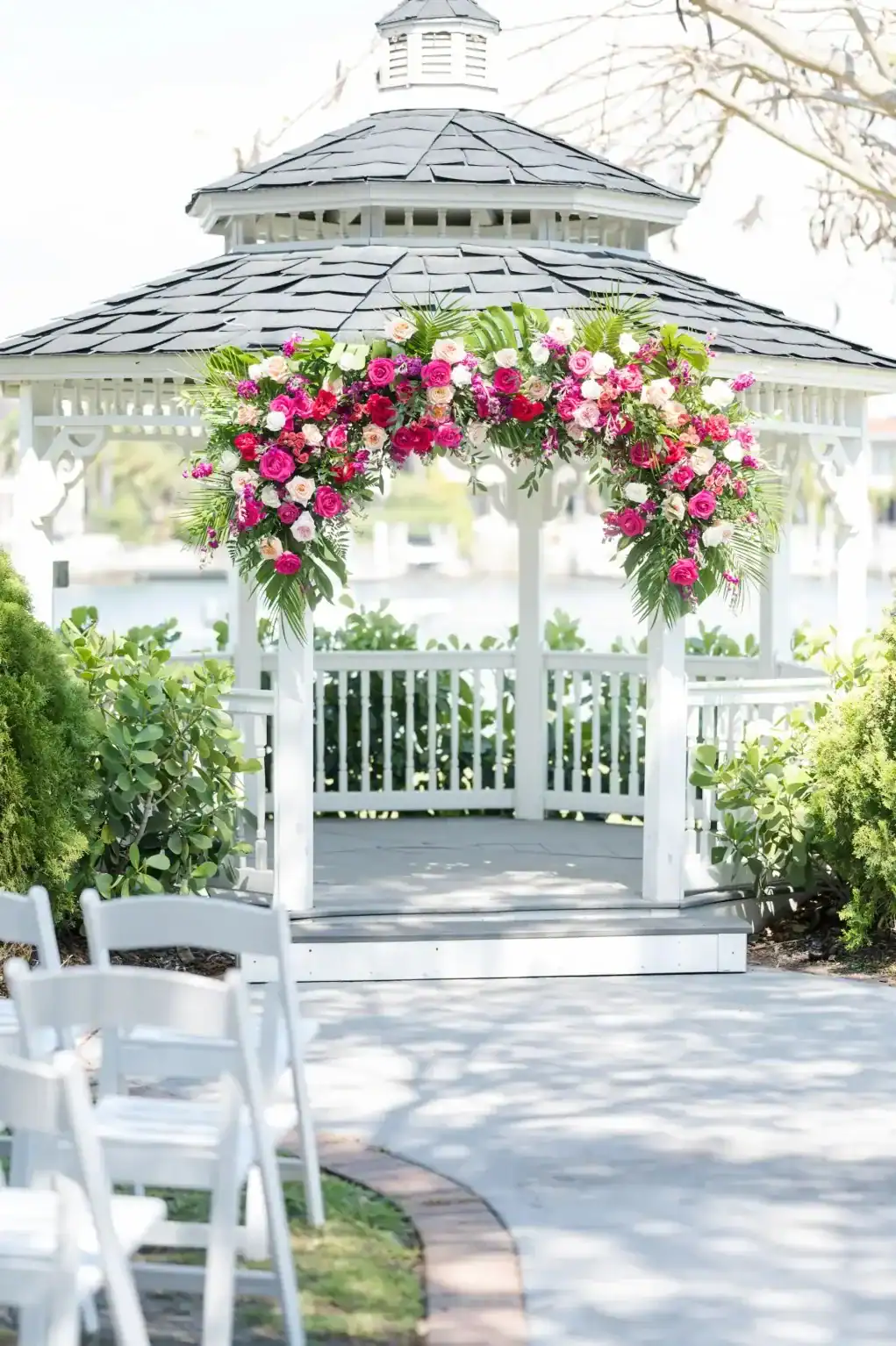 White waterfront gazebo with a vibrant pink, coral, and white floral arch
