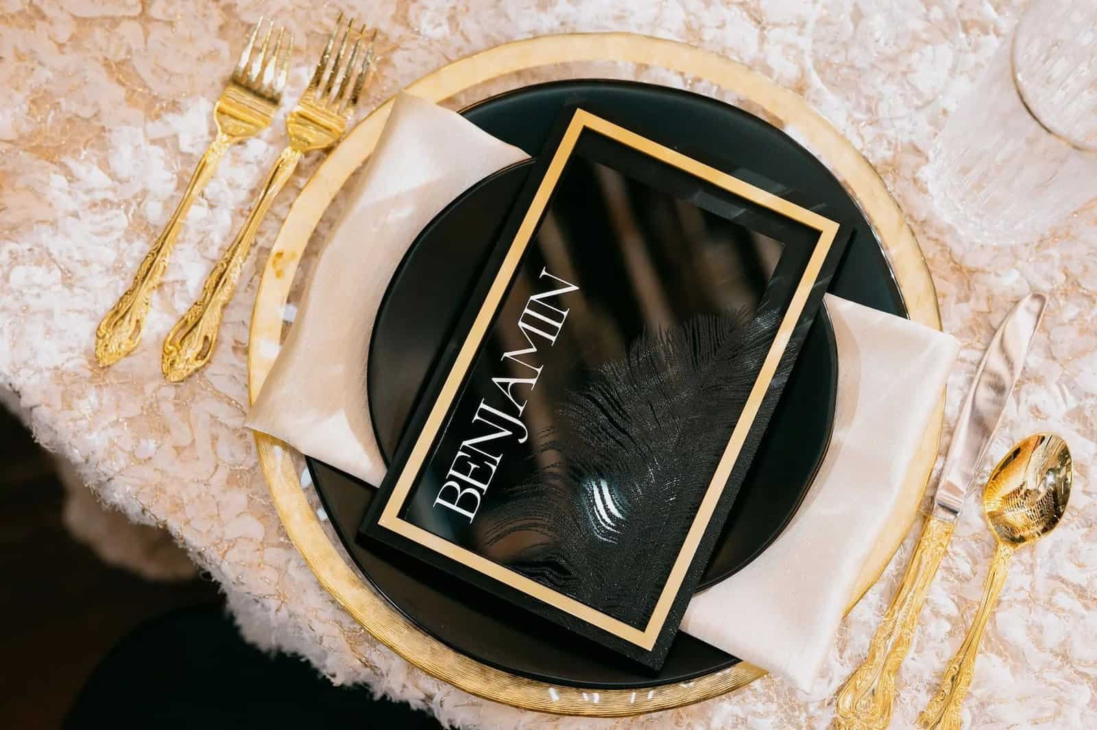 A black and gold place setting has a custom name card resting on textured white linen.