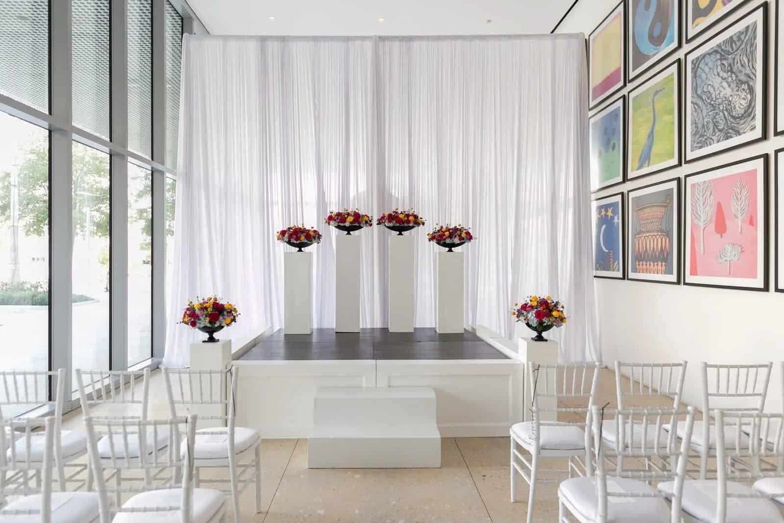 Rows of white chiavari chairs facing the ceremony stage in the museum gallery