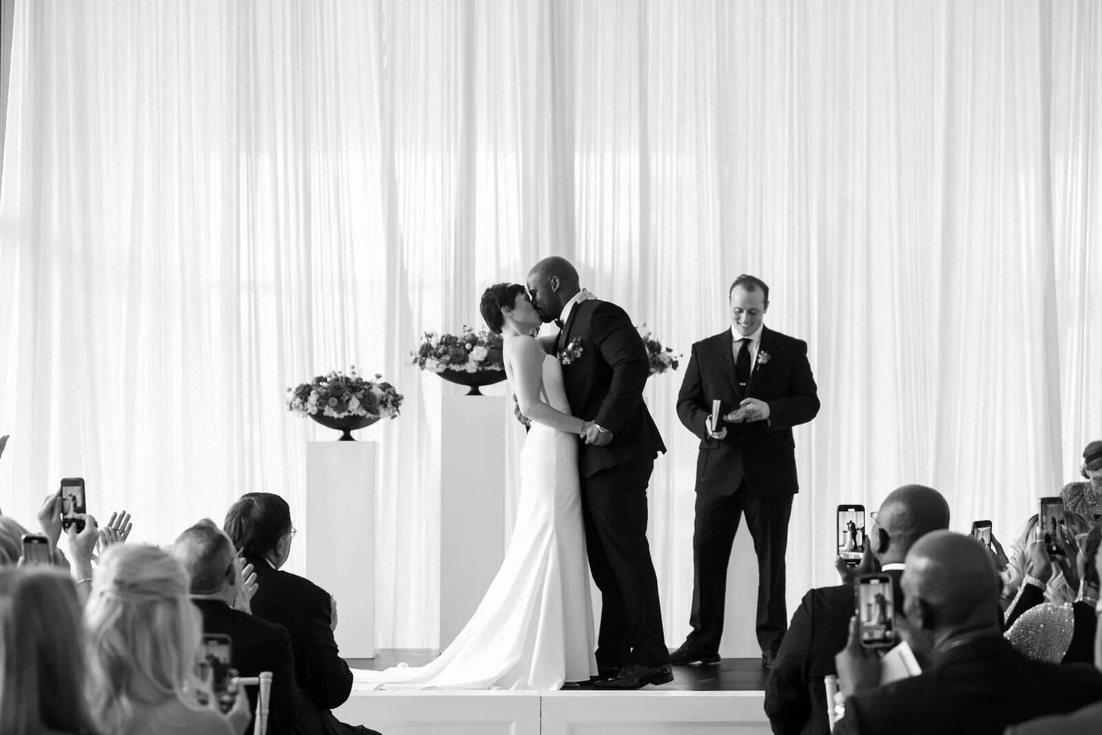Black and white photograph of the couple's first kiss on the ceremony stage