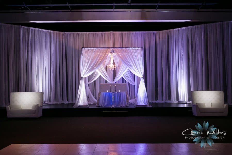 Ornate crystal chandeliers suspended from radial ceiling fabric draping illuminating the reception ballroom