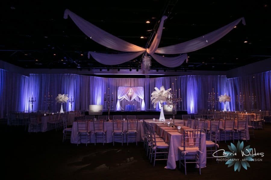 Full ballroom perspective of banquet tables set with gold chiavari chairs, tall floral candelabras, and ambient uplighting