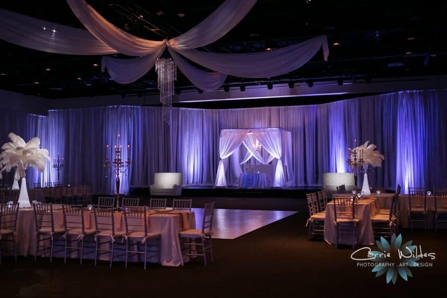 Newlyweds dancing on the polished dance floor beneath radiant ceiling draping and theatrical pin-spot lighting