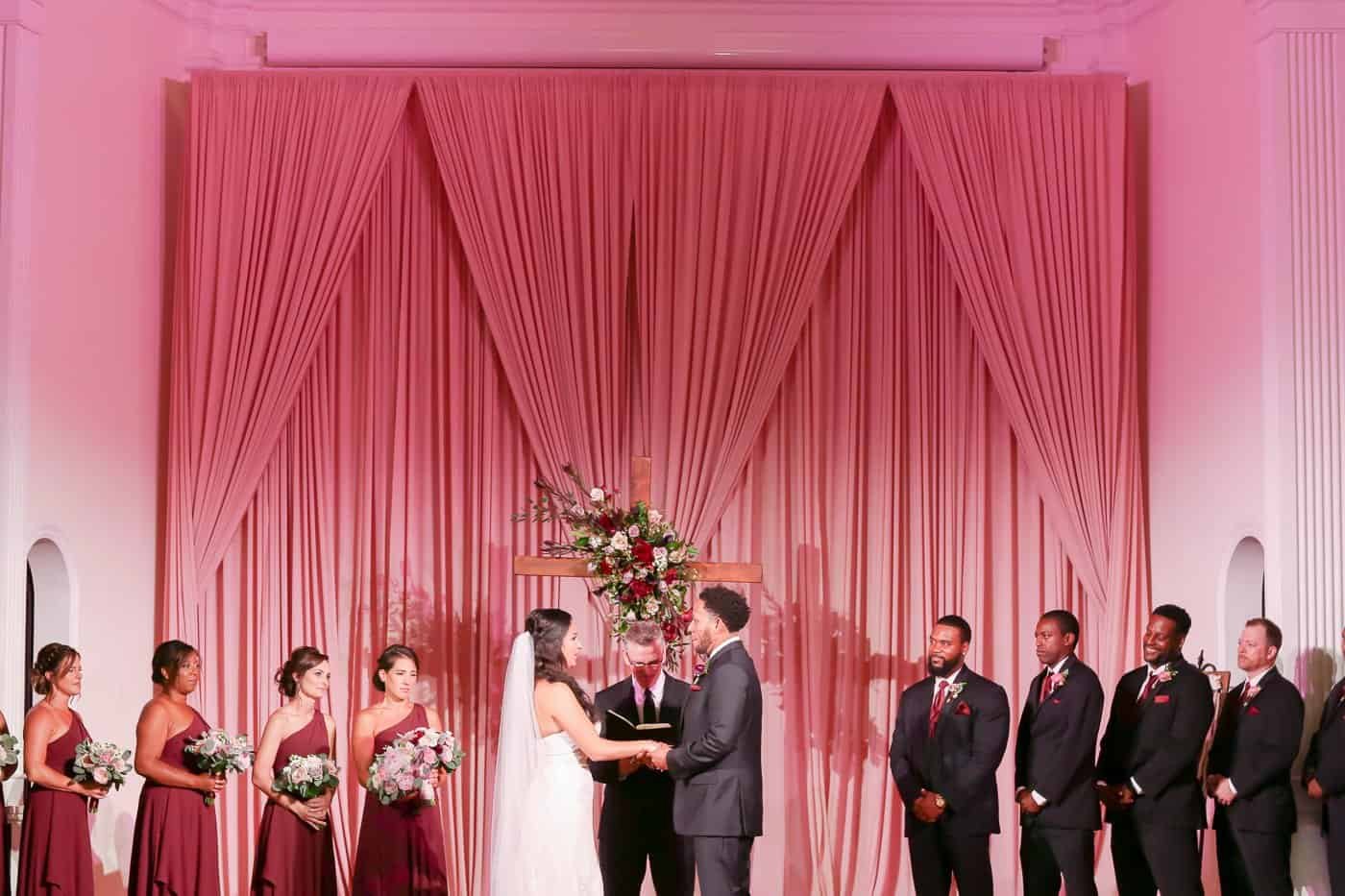 Bride and groom exchanging wedding vows framed by Gabro Event Services custom dusty rose draping