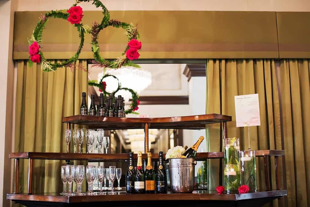 Champagne Bar with Hanging Woven Floral Wreath and Floating Votive Candles Wedding reception champagne bar styling with glass cylinder floating candles and hanging floral wreath decor