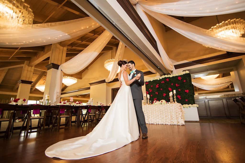 Couple First Dance Beneath Custom Ballroom Ceiling Draping Bride and groom sharing first dance in the Countryside Country Club ballroom beneath flowing white ceiling fabric and fairy lighting
