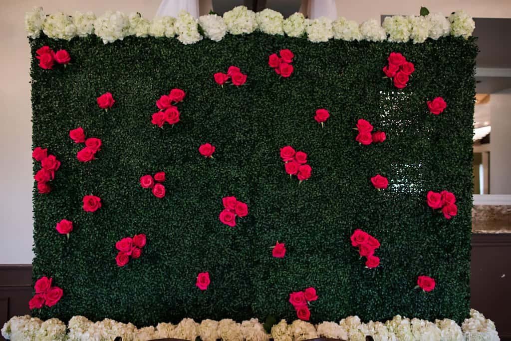 Custom Flower Wall Backdrop with Roses and Greenery at Sweetheart Table Lush floral wall backdrop with white hydrangeas, red roses, and vibrant greenery behind sweetheart table by Gabro Event Services