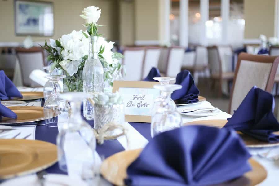 Reception feasting table detail with fresh ferns, rose gold votives, marble menus, and white porcelain plates at Countryside Country Club