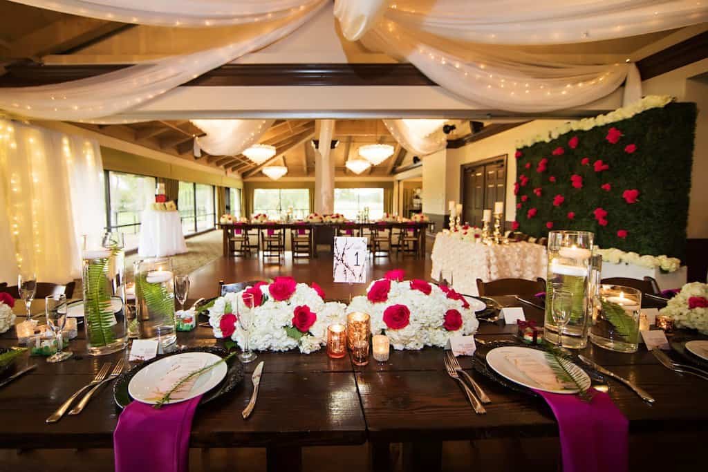 Reception Feasting Tablescape with Black Chargers and Floating Candle Vases Long wooden banquet feasting table setup with cylinder floating candle vases, black charger plates, and jewel-toned floral accents