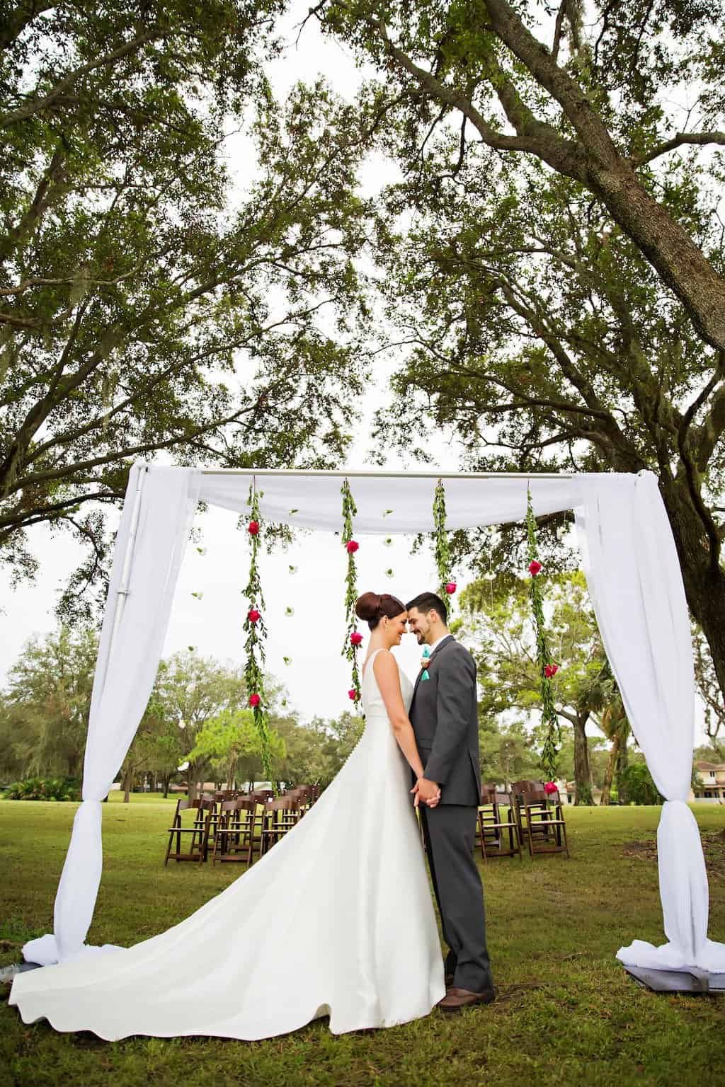 Wedding Ceremony Couple Portrait at Outdoor Draped Arch Countryside Country Club Bride and groom portrait under custom white draped ceremony arch with floral garlands at Countryside Country Club in Clearwater