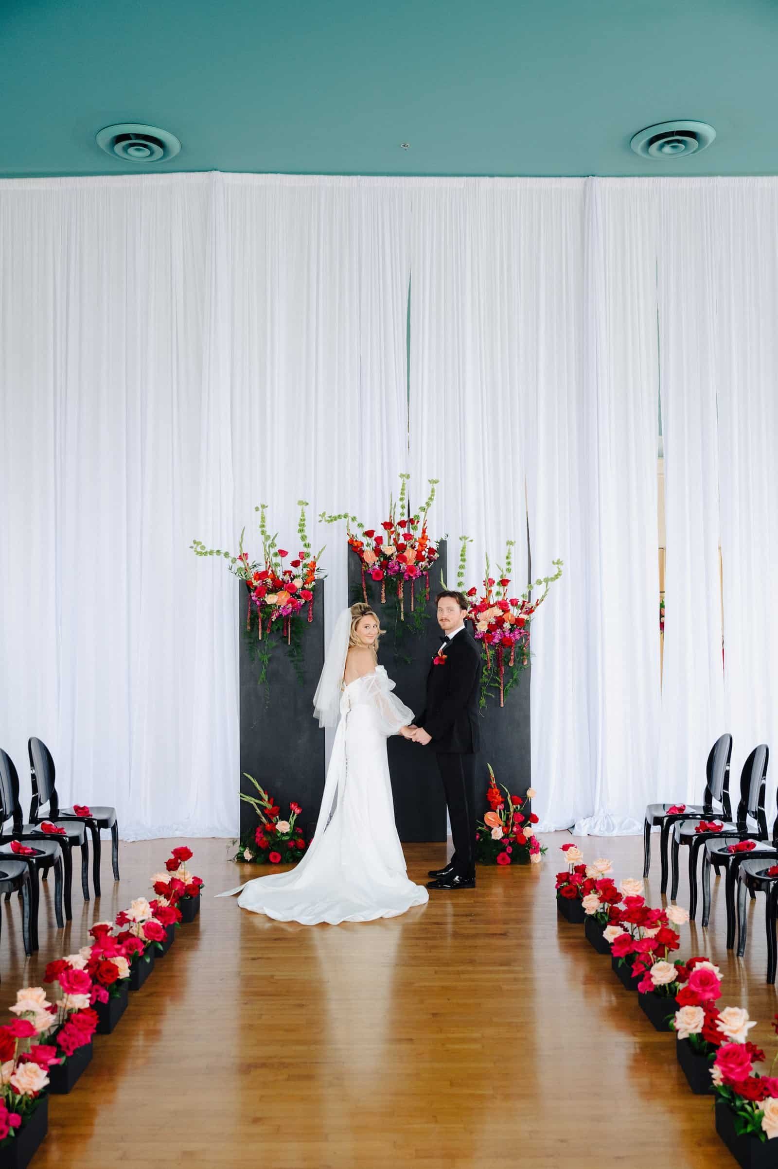 Modern runway style wedding ceremony seating with sleek black chairs and florals.
