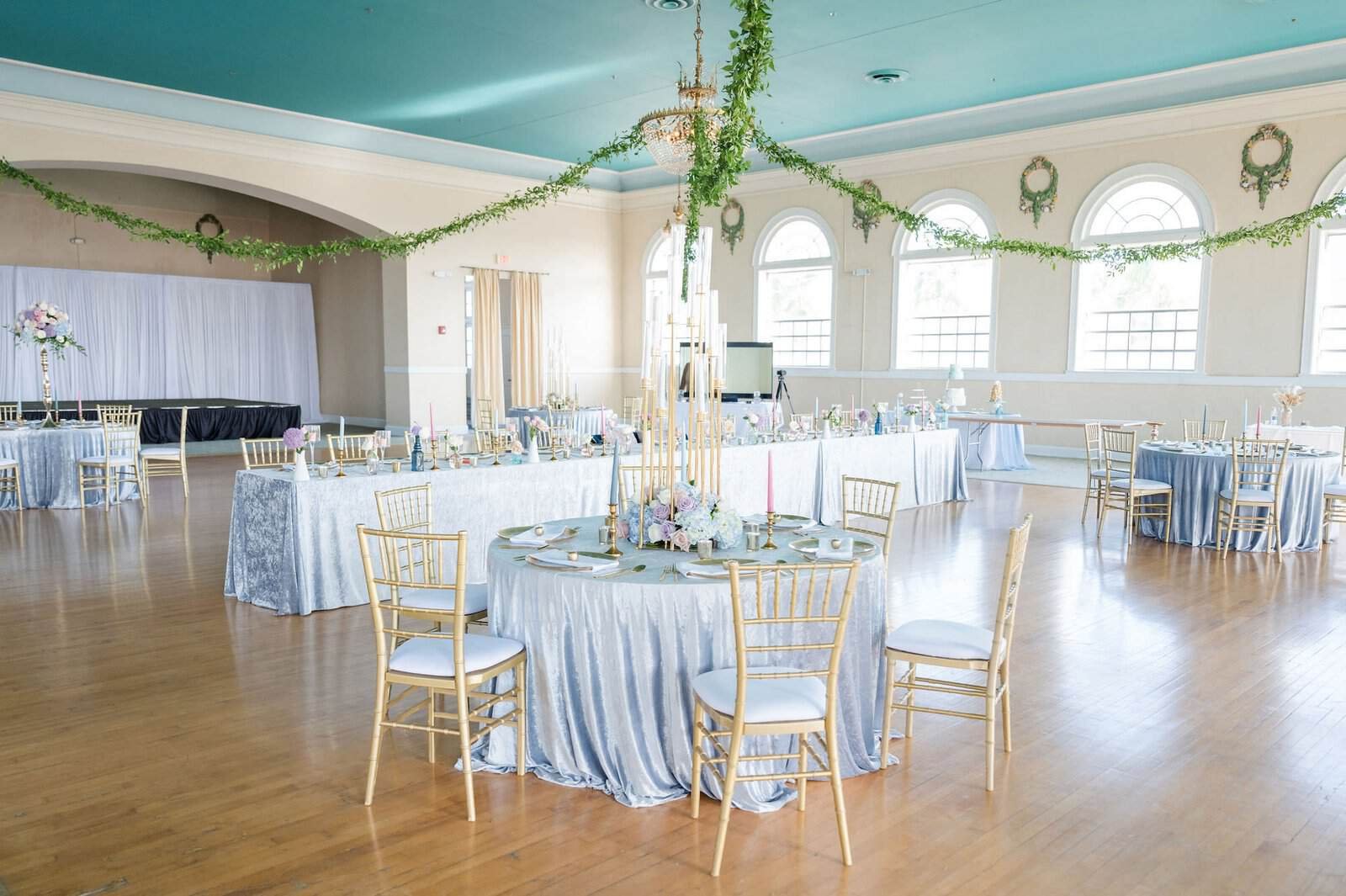 Spring pastel blue reception feasting table with gold chiavari chairs and sky blue velvet linens from Gabro Event Services