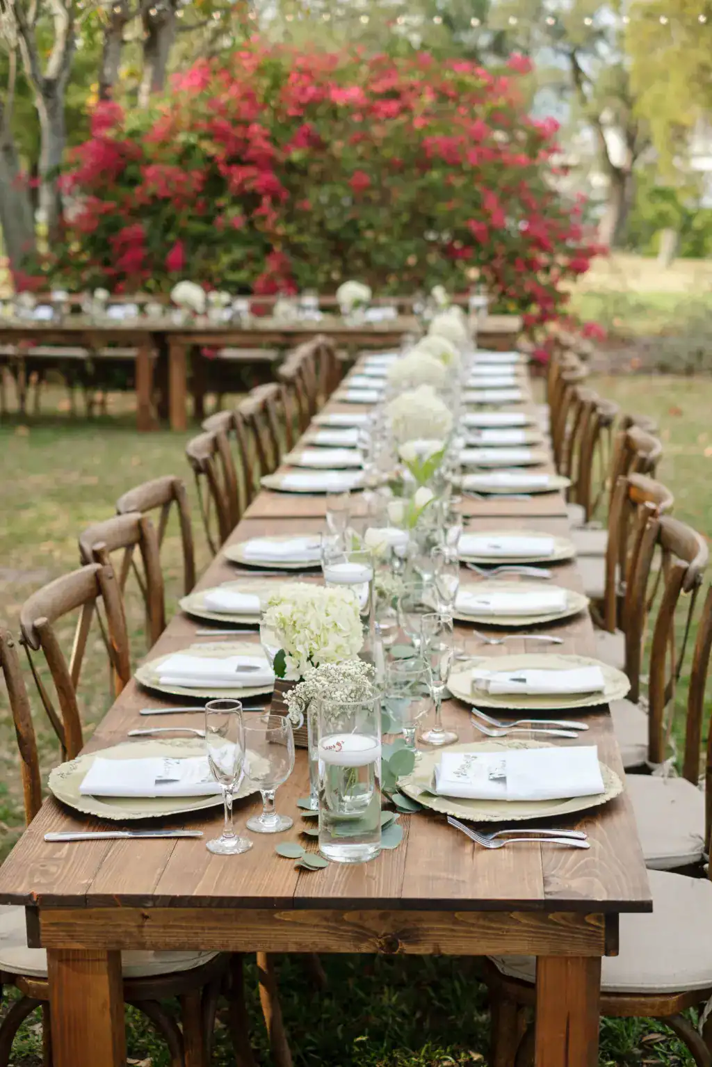 Bare wood farm table set with white place settings and a greenery runner