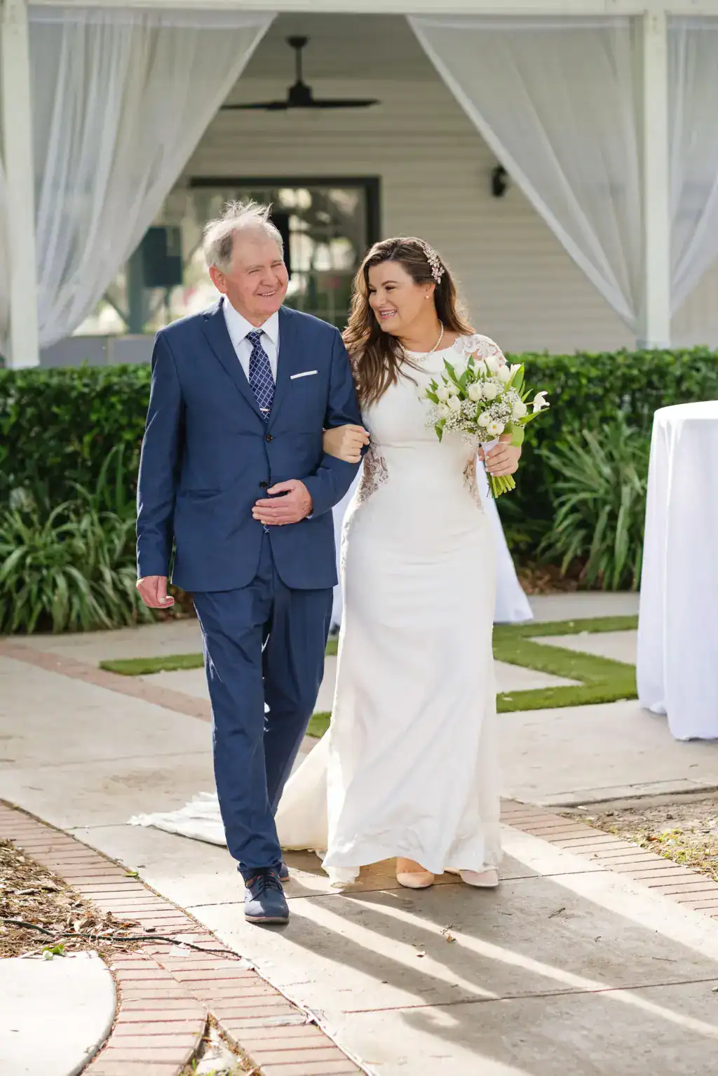 Bride in elegant lace gown walking through lush tropical garden pathway at Davis Island