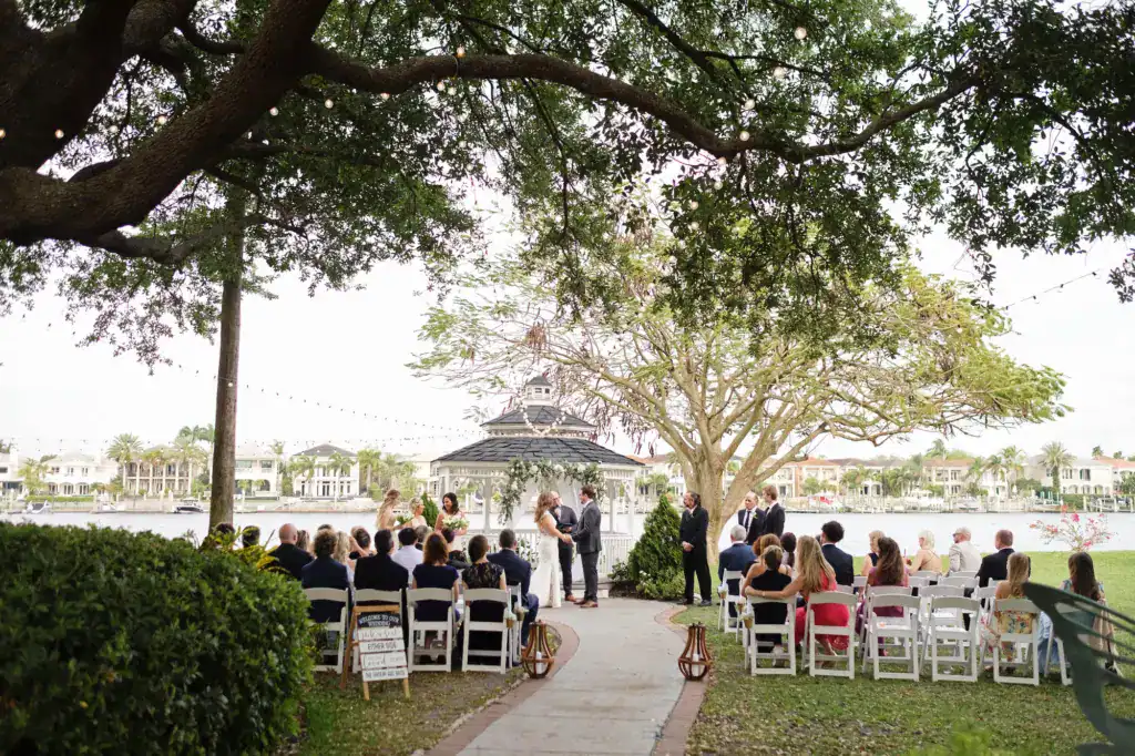 Waterfront garden ceremony lawn with wooden arbor, floral arrangements, and white garden guest seating