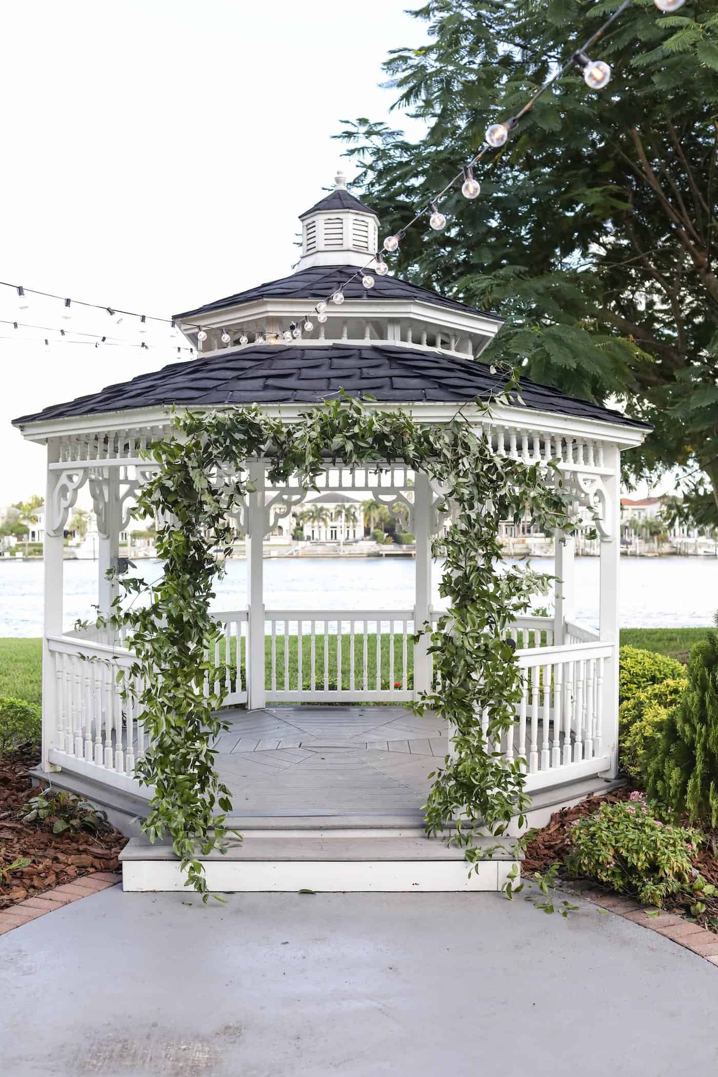 Outdoor waterfront ceremony setup at Davis Islands Garden Club with greenery-draped white gazebo overlooking Hillsborough Bay in South Tampa
