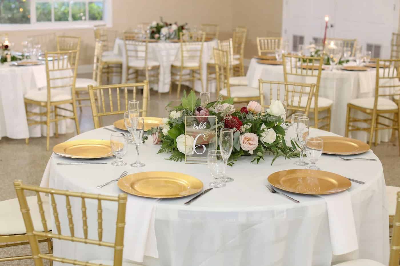 Classic South Tampa wedding reception at Davis Islands Garden Club featuring round tables with gold Chiavari chairs, gold chargers, and floral centerpieces by Gabro Event Services