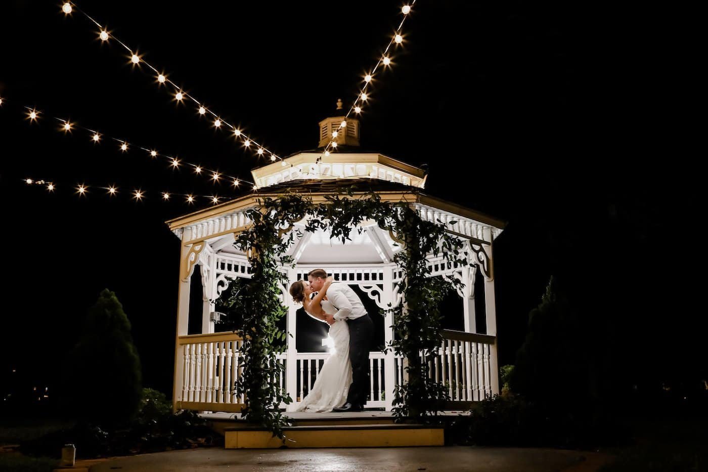 Lexi and Tucker sharing a romantic nighttime wedding portrait under the Davis Islands Garden Club gazebo illuminated with bistro string lights by Gabro Event Services