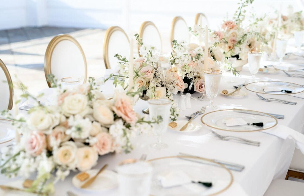 Long banquet feasting table styled with lush blush floral arrangements, gold flatware, and ambient candle illumination