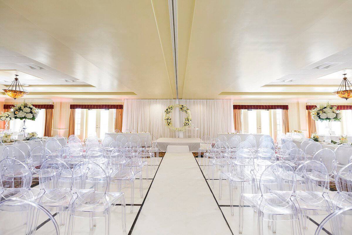 Travel-themed Clearwater Beach wedding ceremony decor with white draping and ghost chairs at Duval Ballroom Center