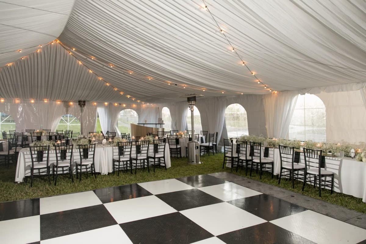 White pleated tent draping and bistro string lighting above a black and white checkered dance floor at The Fenway