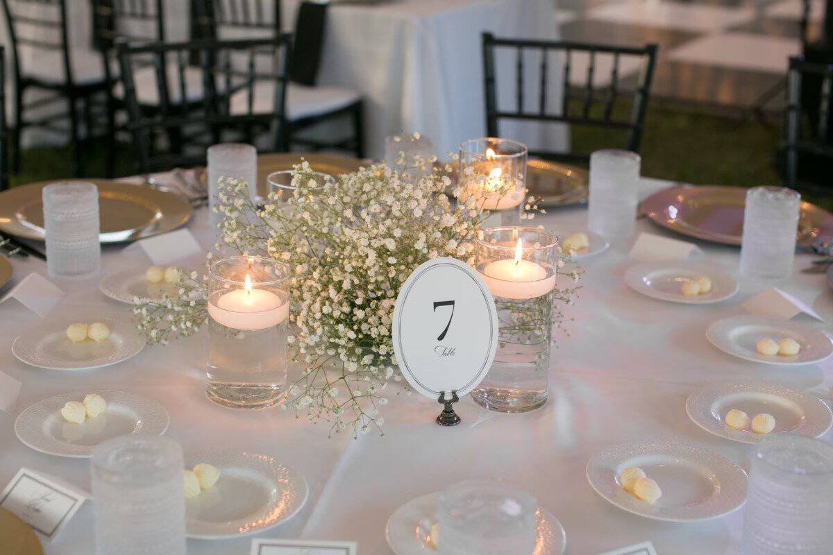 Round reception table set with a white linen, glass chargers, pillar candles and a black and white table number