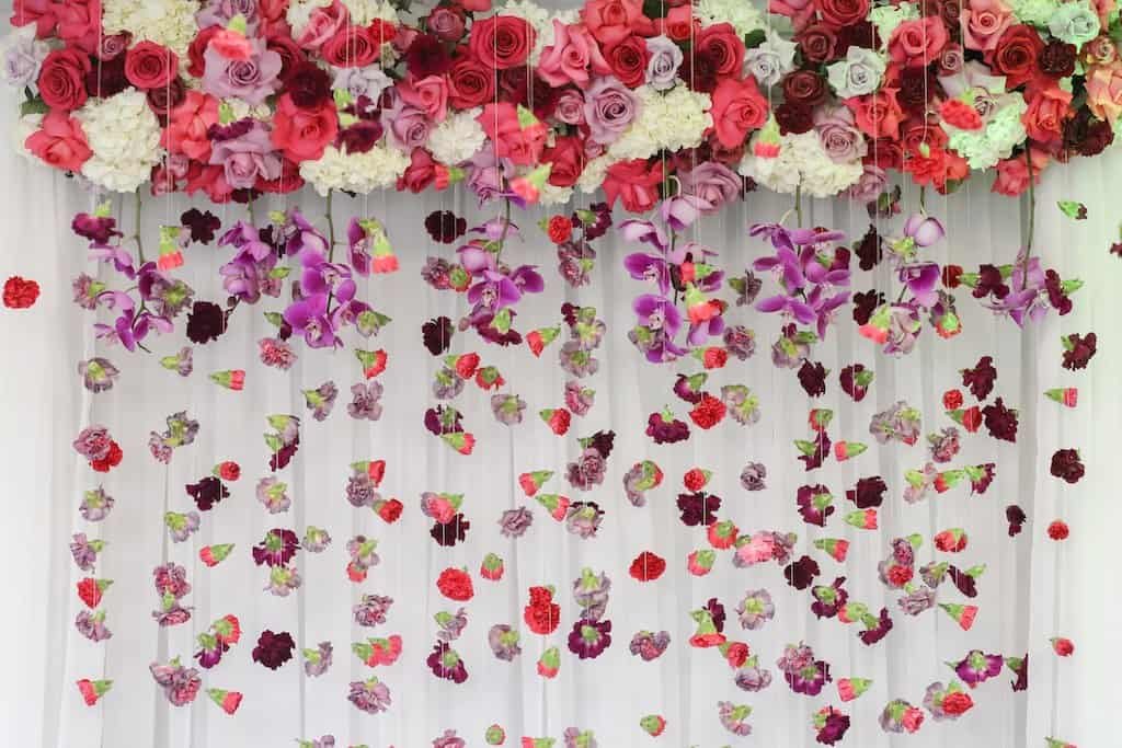 Lush wedding ceremony arch bursting with purple orchids, pink roses, hanging carnations, and crystal bead accents