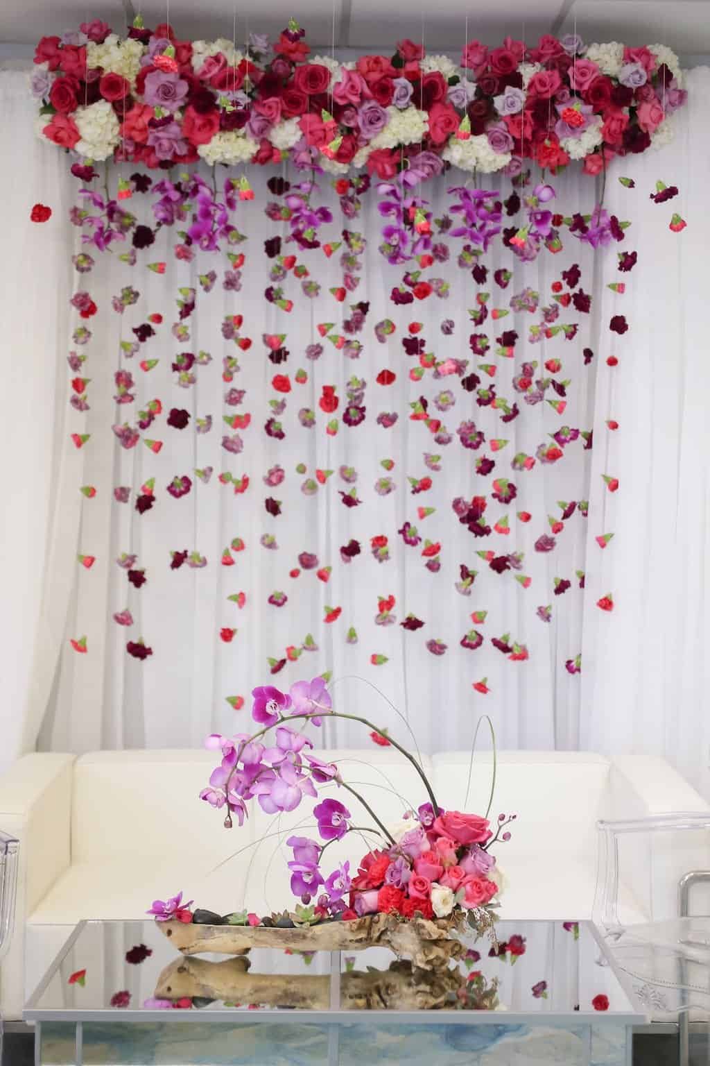 Opulent wedding reception tablescape illuminated with magenta uplighting beneath a floating suspended floral centerpiece