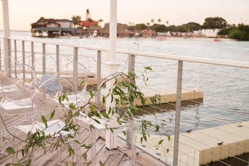 Waterfront wedding ceremony at The Godfrey Tampa featuring clear acrylic ghost chairs and eucalyptus aisle garland