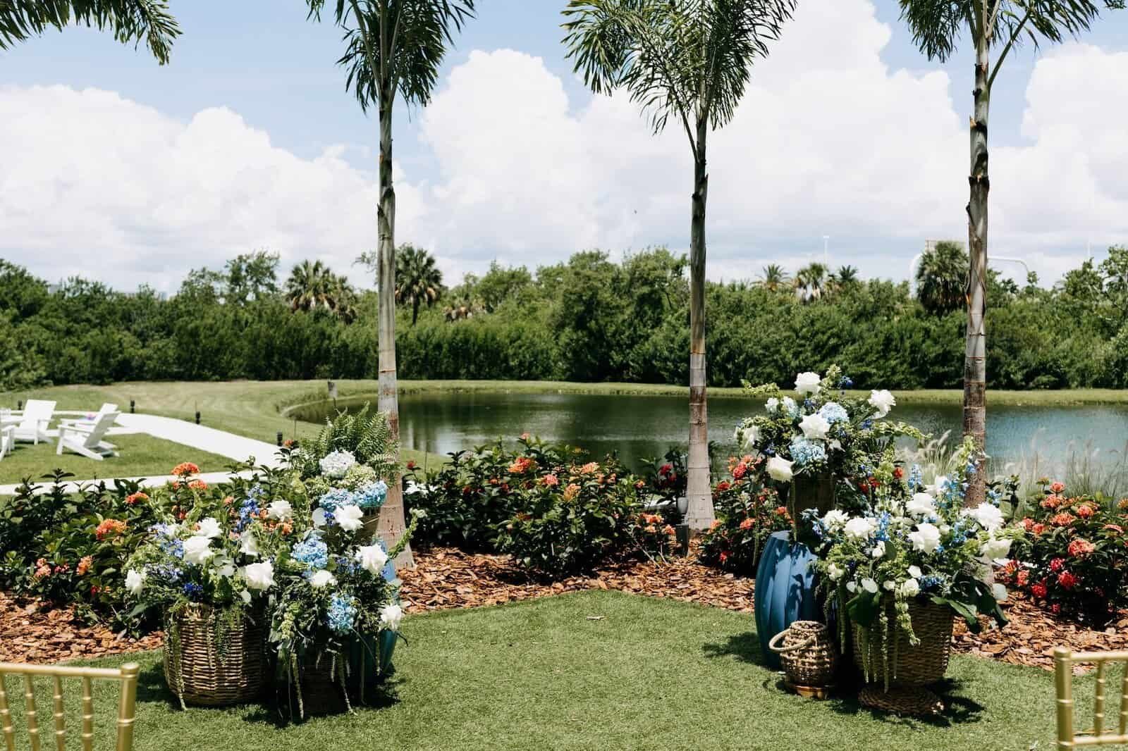 Gold chiavari chairs arranged for a ceremony on the lawn with palm trees and water behind