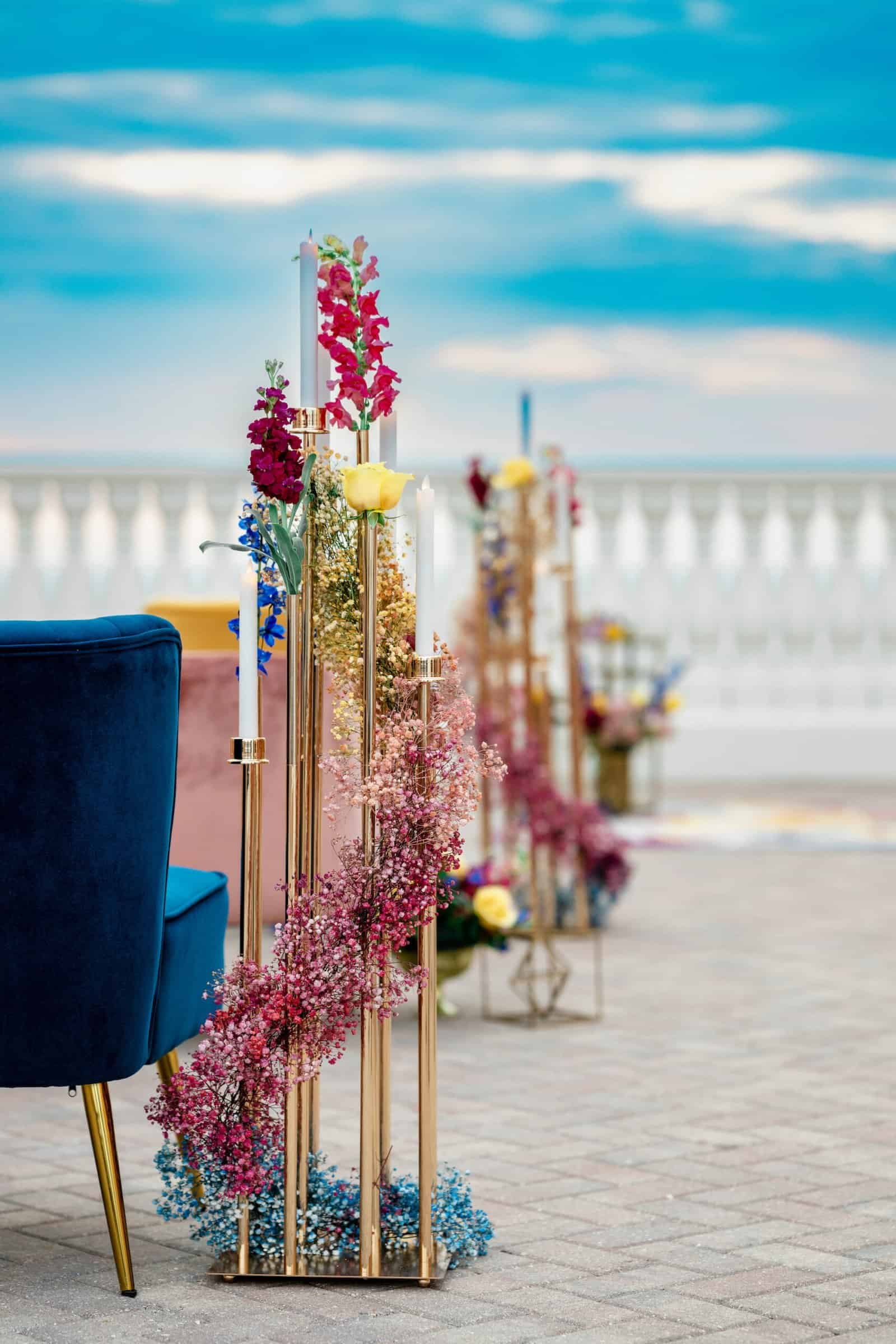 Modern gold geometric candelabras surrounded by vibrant floral arrangements on a wedding table.