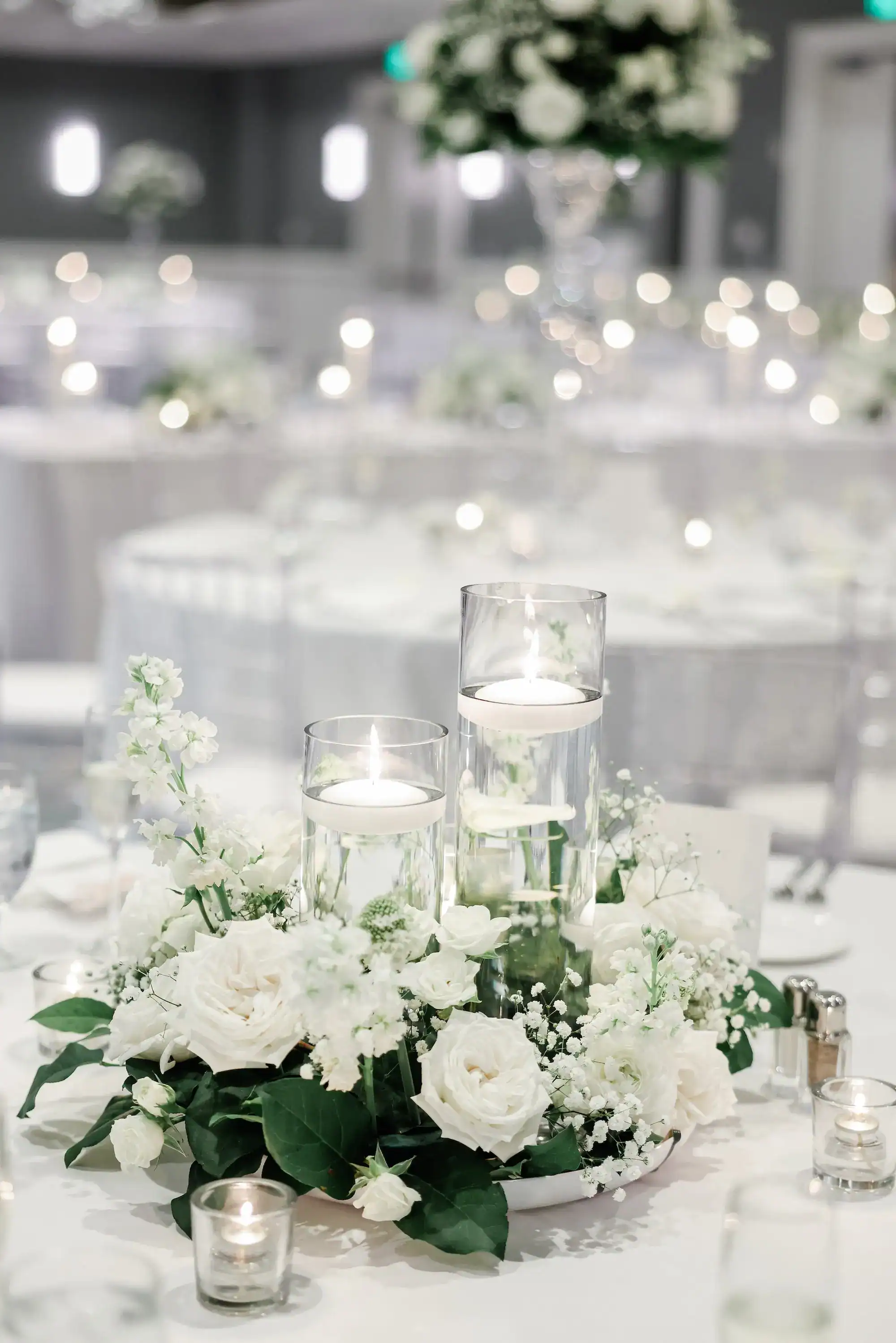 Romantic candlelit wedding reception tablescape detail with floating pillar candles and white roses