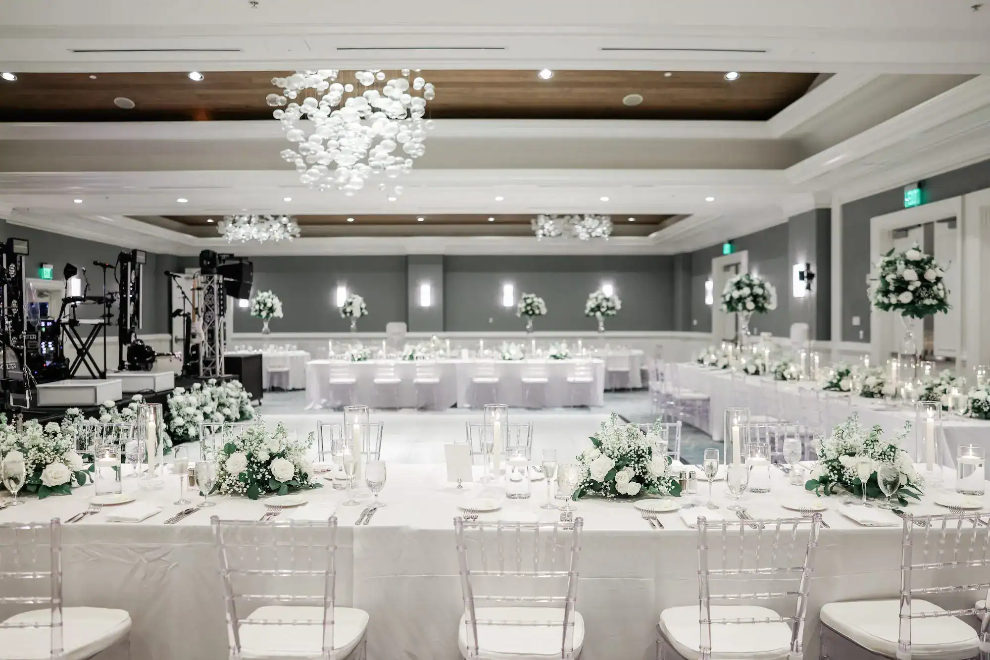 Monochromatic white ballroom reception featuring Gabro Event Services perimeter draping and clear Chiavari chairs