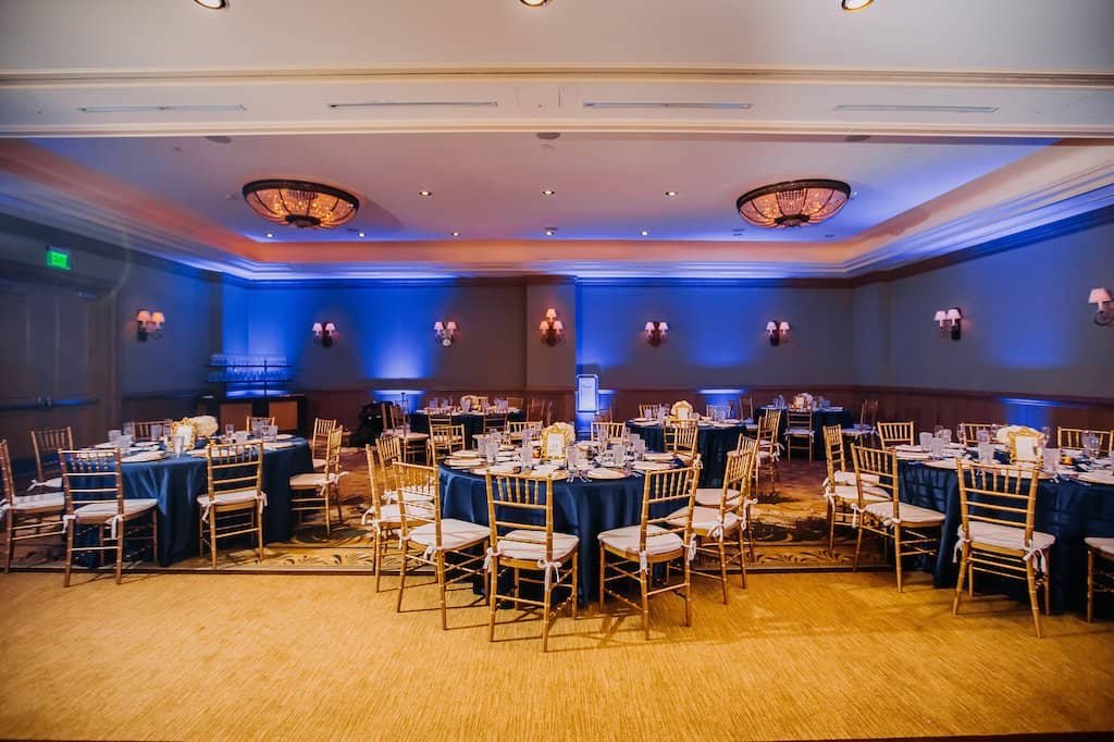 Detailed view of wedding reception dining table with gold chiavari chairs, navy tablecloths, and elegant gold rimmed glassware
